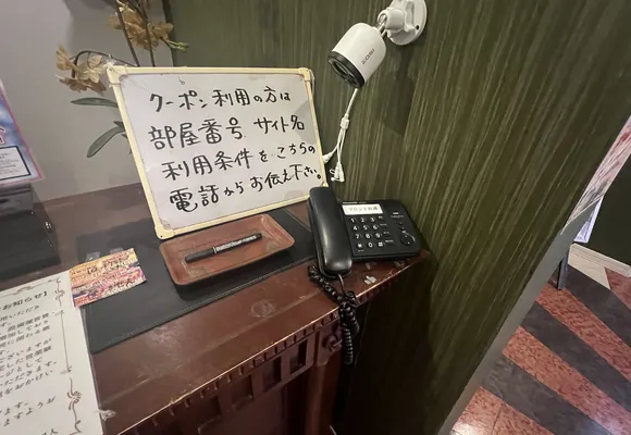 ロビーカウンターの直通電話と立て札。クーポンをご利用の方は、お部屋番号・サイト名・利用条件をこちらのお電話でお伝えください、と書いてあります